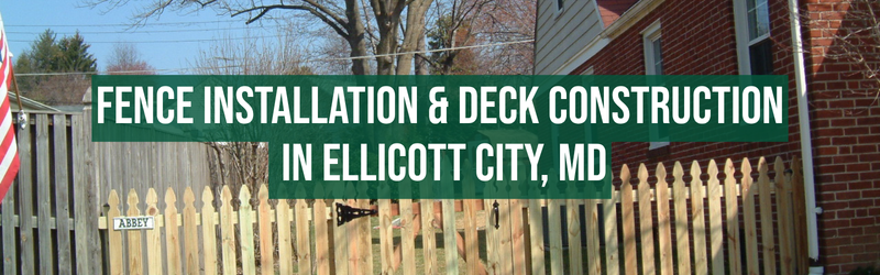 A wooden fence with a small sign that reads "ABBEY." In the background, there are trees, a house with red brick walls, and a neighboring house. Overlaid on the image is a green banner with white text that says "FENCE INSTALLATION & DECK CONSTRUCTION IN ELLICOTT CITY, MD."
