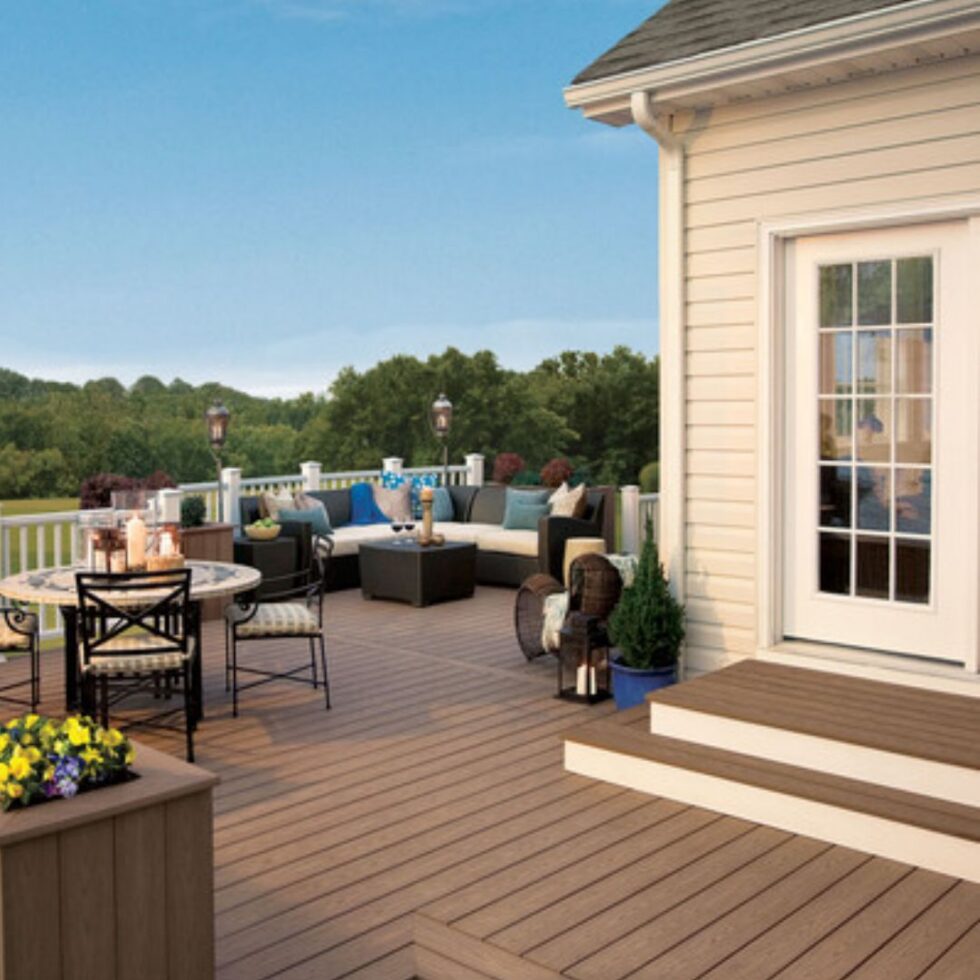 Spacious composite backyard deck with outdoor dining furniture, lounge seating, white railings, and scenic views attached to a residential home.