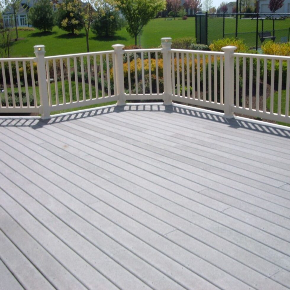 Spacious gray composite deck with white vinyl railings overlooking a landscaped backyard in a residential neighborhood.