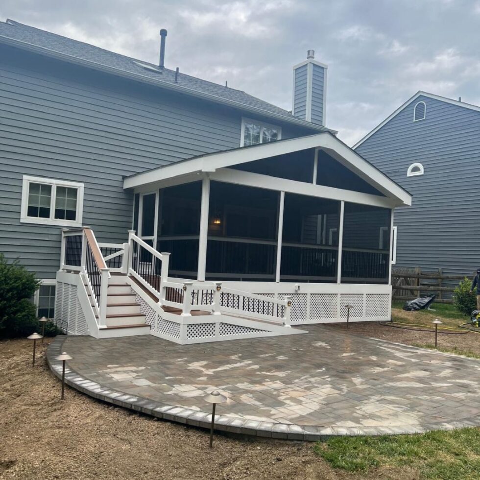 Custom screened porch with composite decking, white railings, staircase access, and an adjoining paver patio attached to a residential home.