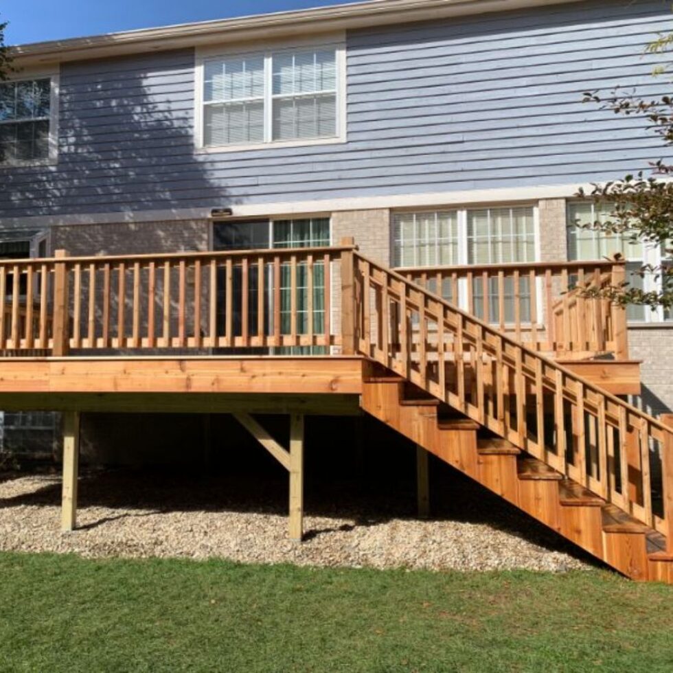 Custom elevated wooden deck with full-length staircase, safety railings, and sliding door access attached to a multi-story residential home.