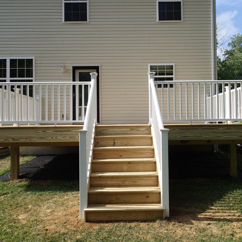Custom elevated wood deck with white vinyl railings, center staircase, and backyard access attached to a two-story residential home.