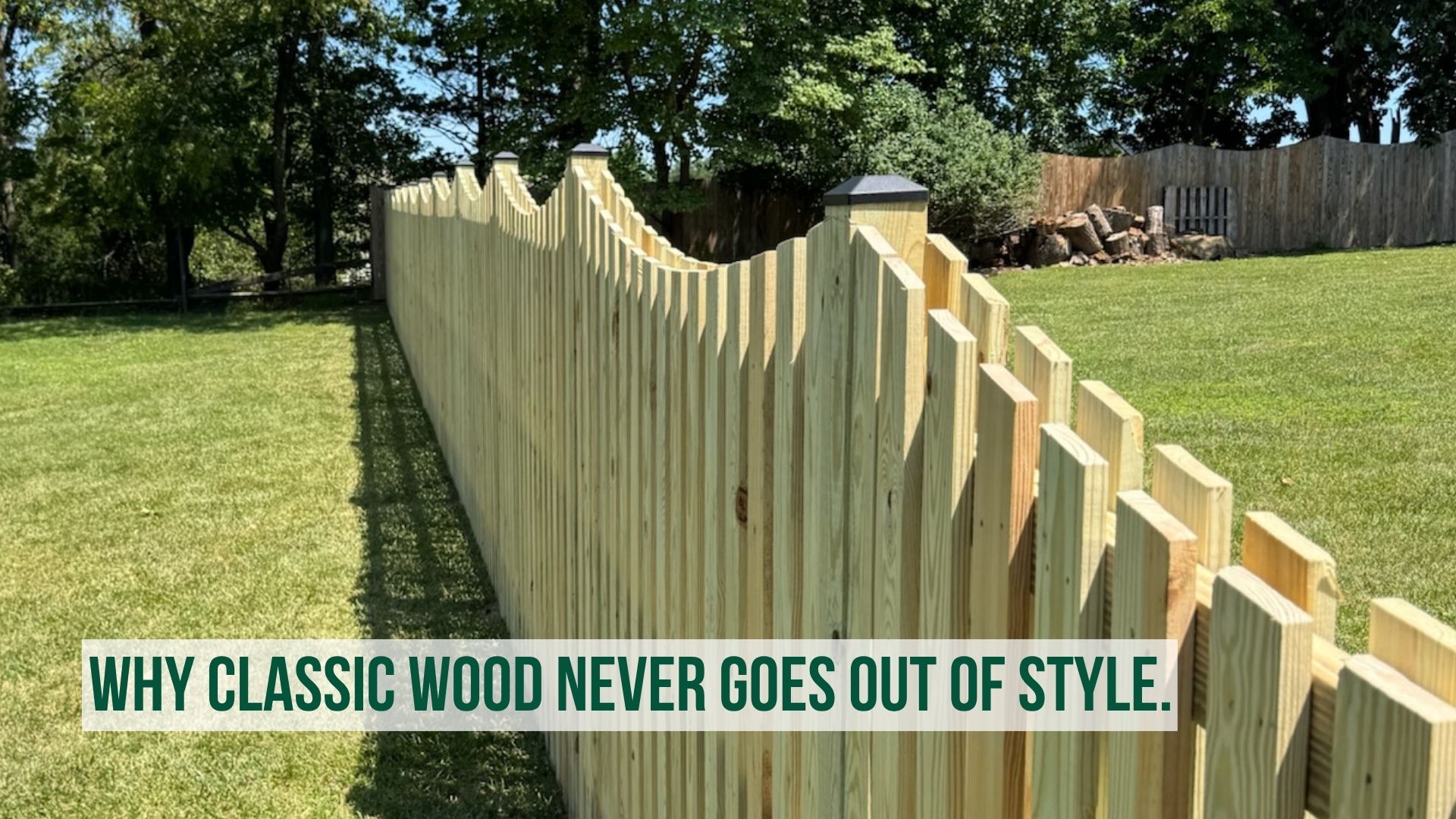 Traditional wooden scalloped privacy fence showing natural wood grain texture and vertical panels bordering a vibrant green backyard